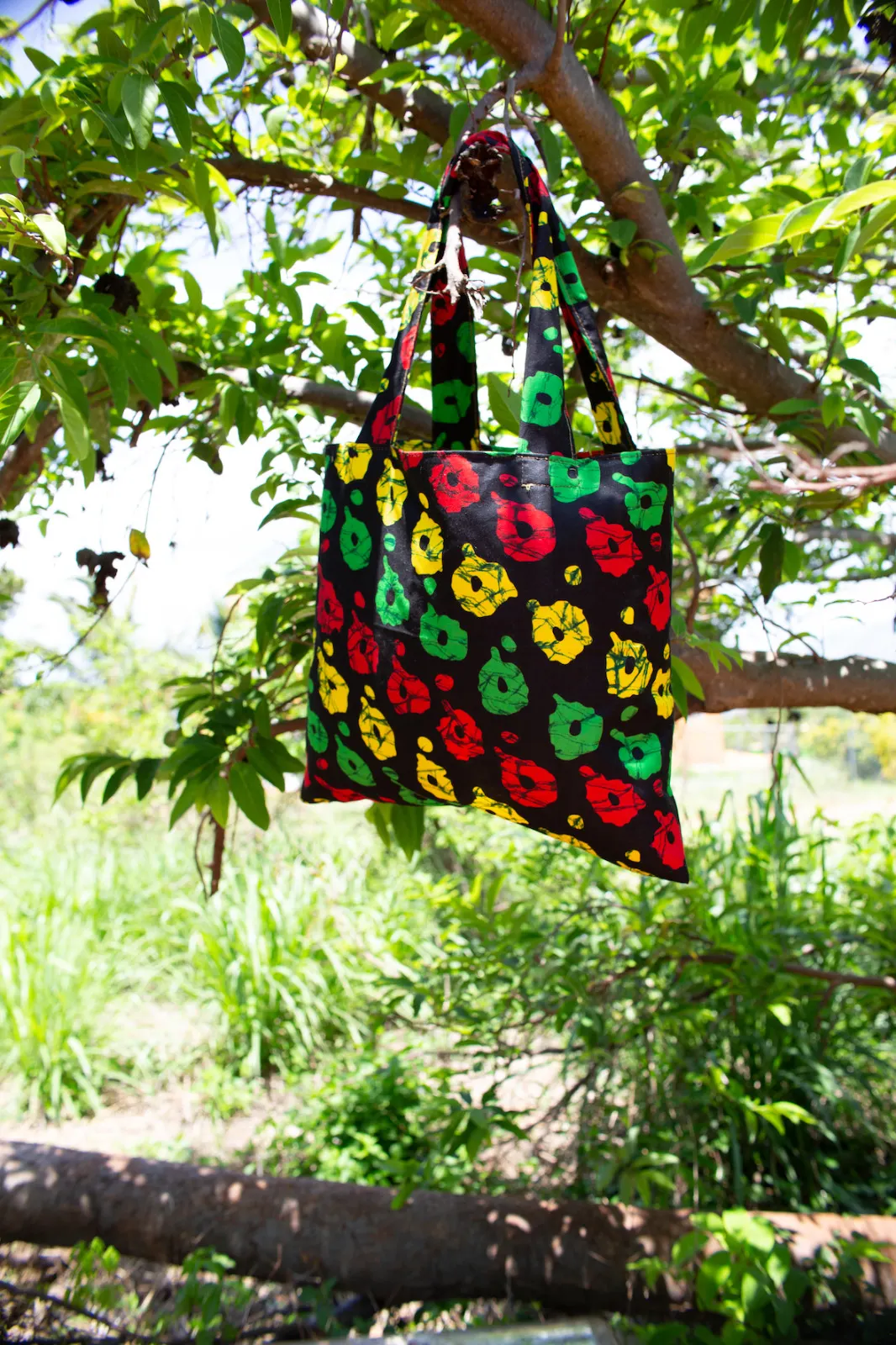 A tote bag in black African-print fabric with red, yellow and green, hanging from a tree