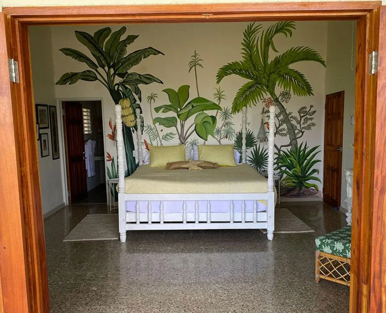 A mural of banana plants, palms and tropical leaves painted on a bedroom wall behind a white four-poster bed