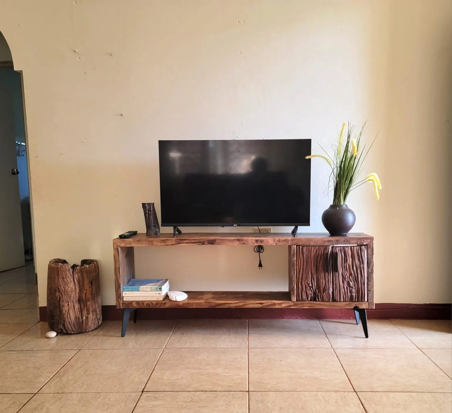 A rustic wooden TV stand on black metal legs, with rough-hewn wooden doors