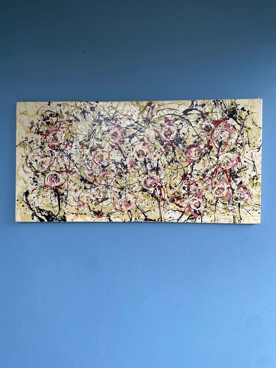 A drip painting in cream, pink, red and black, hanging on a blue wall