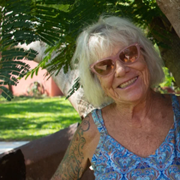 Ronda Benett, smiling, in pink sunglasses under a tree