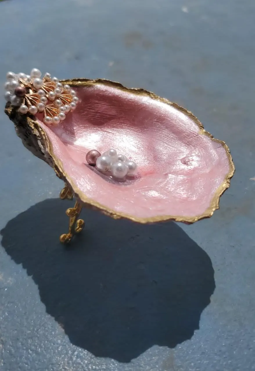 A pink oyster shell dish on gold feet, with pearls and a gold edge