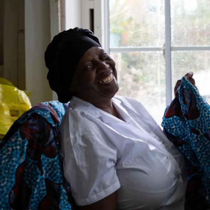 Terry Moxam, laughing, holding printed fabric at her sewing table