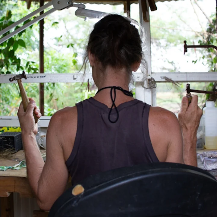 At the jeweller’s bench, seen from behind, hammer in hand