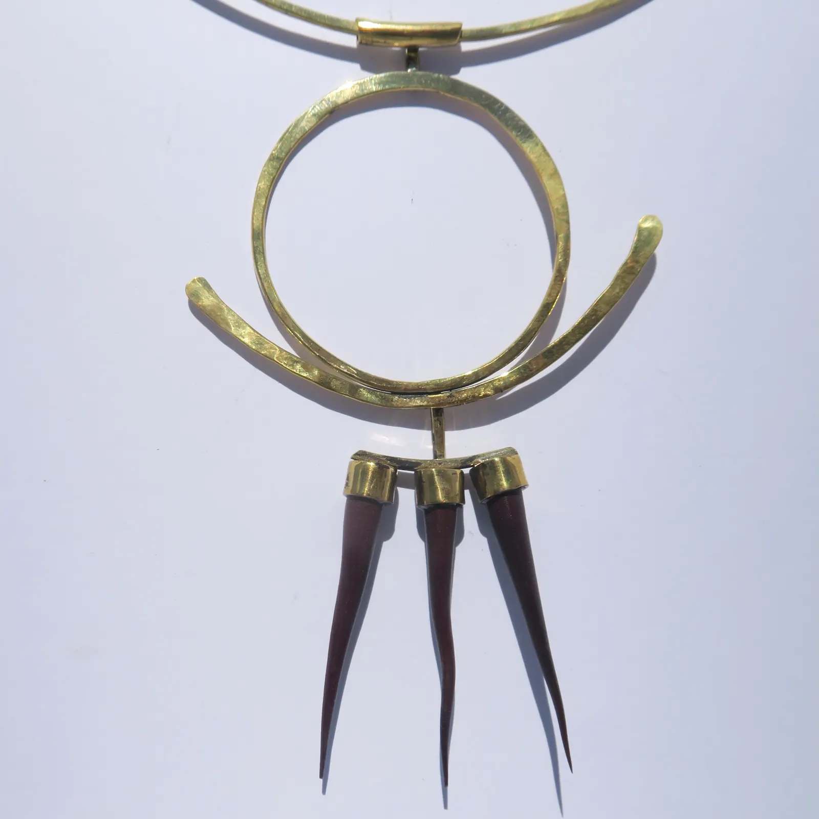 “Dragon” (2023): a hammered brass pendant on a neck ring, with three wooden claws