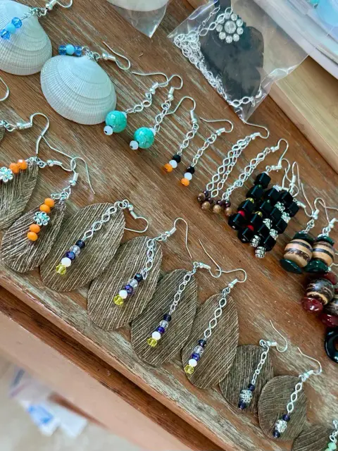 Earrings laid out on a wooden table: shells, turquoise beads, crystal drops on textured metal leaves, and wooden beads