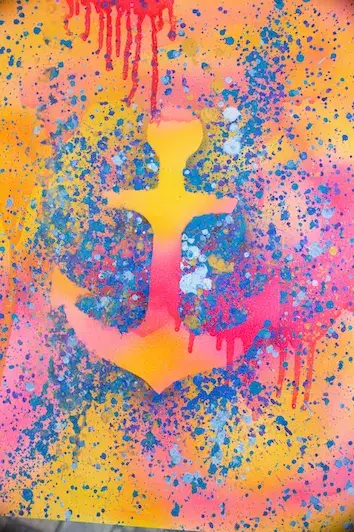 A yellow anchor spray-painted over splashes of pink, orange and blue