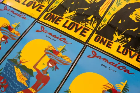 Painted panels side by side: “Jamaica One Love”, a woman carrying fruit against a yellow sun, and “One Love” in black on yellow, signed Dennis Di Artist