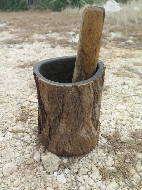 A wooden mortar and pestle, the mortar carved from a tree trunk with its bark left on