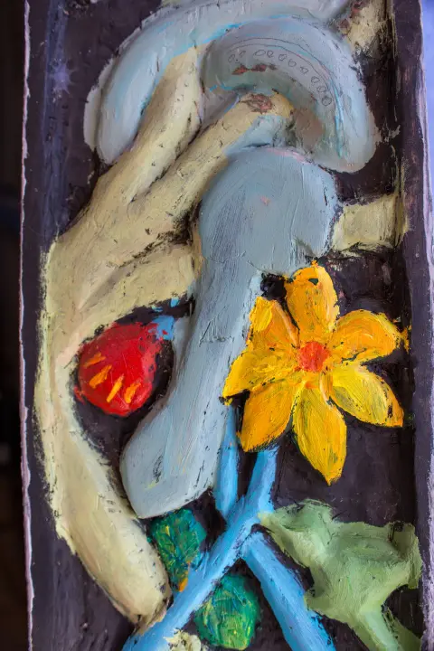 A carved wooden relief painted with a figure and a yellow flower