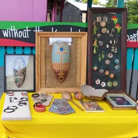 Her stall: calabash masks in frames, a board of earrings and beaded bracelets on a yellow table