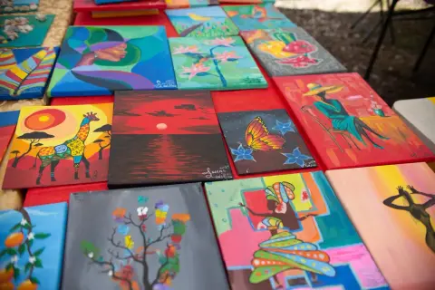 A table of his paintings: a giraffe, a red sunset, a butterfly, a woman in a hat, and more, signed Lucas Williams