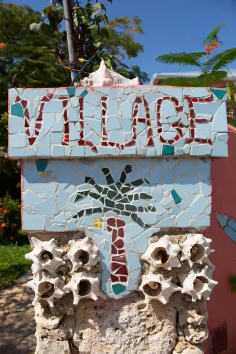 A mosaic sign reading “Village” with a palm tree, above a row of conch shells