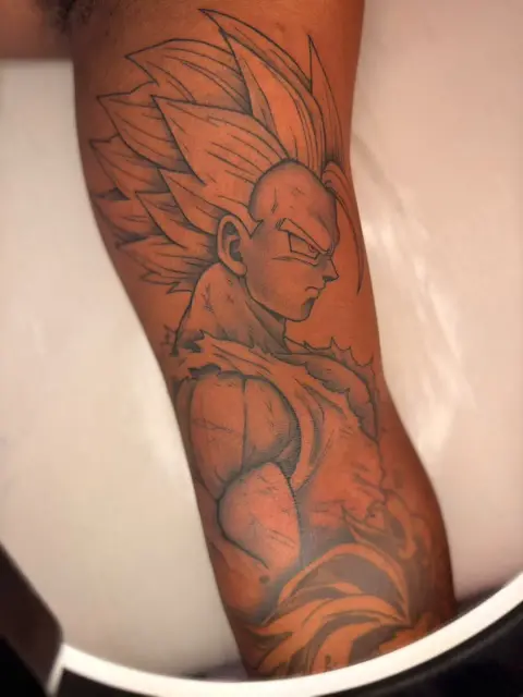 A shaded line tattoo of an anime warrior with spiky hair, on an upper arm