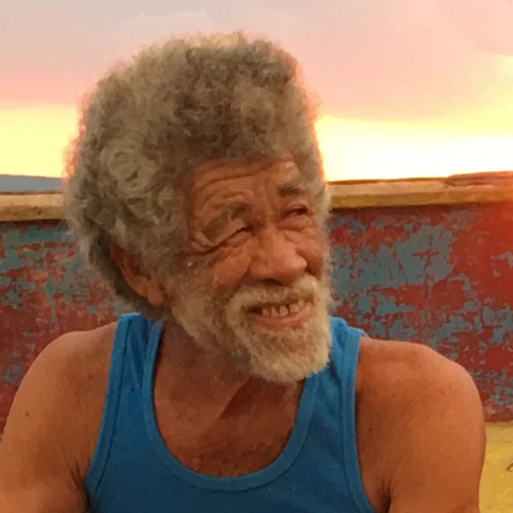 Tommy Wong, smiling, by a painted boat at sunset
