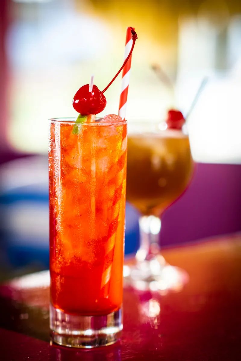 Beyond Sunset Bar and Smoke Grill — A tall red cocktail with ice, a cherry and a striped straw