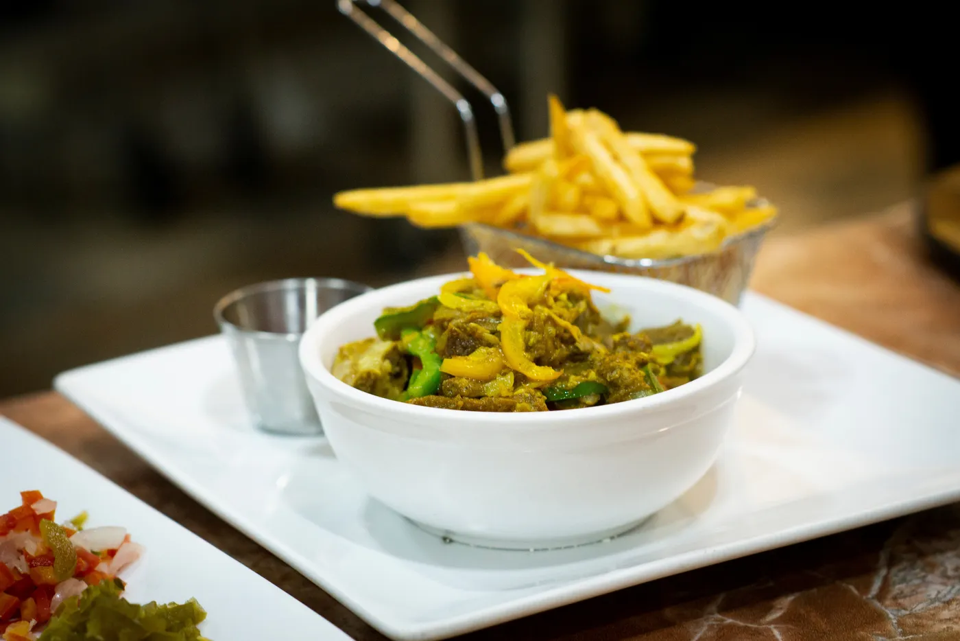 Beyond Sunset Bar and Smoke Grill — A bowl of curry with peppers and onions, beside a basket of fries and a small side of salad