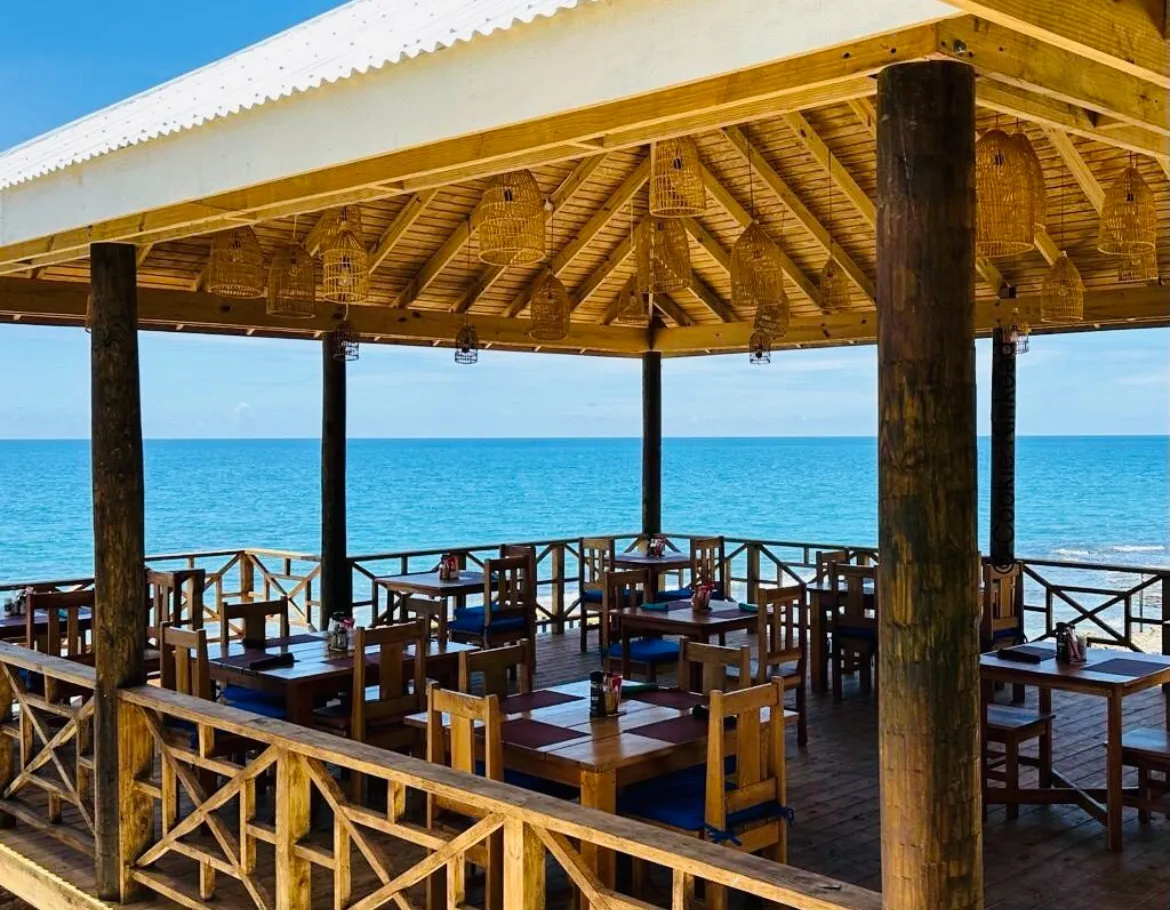 The open-air restaurant deck by day, with wooden tables and chairs under a roof hung with woven lamps, and the blue Caribbean Sea beyond