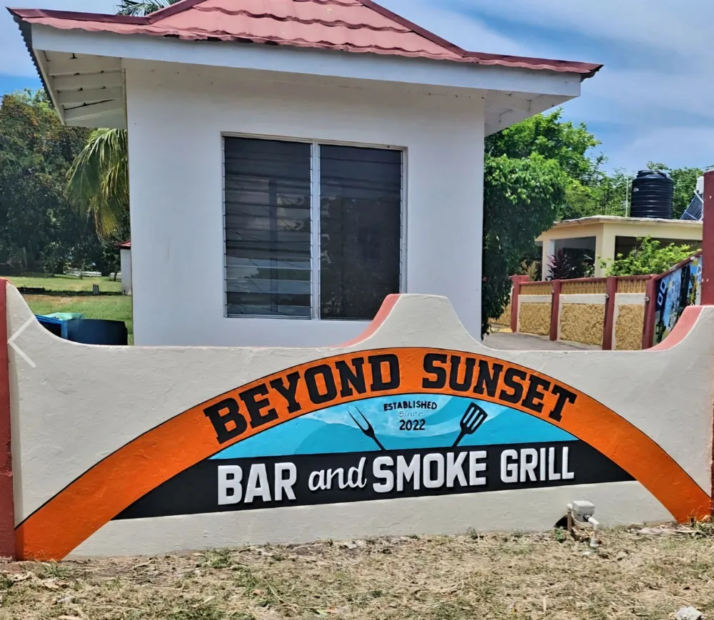 The Beyond Sunset Bar and Smoke Grill sign, established 2022, painted on a white wall at Beyond Sunset Resort and Villas