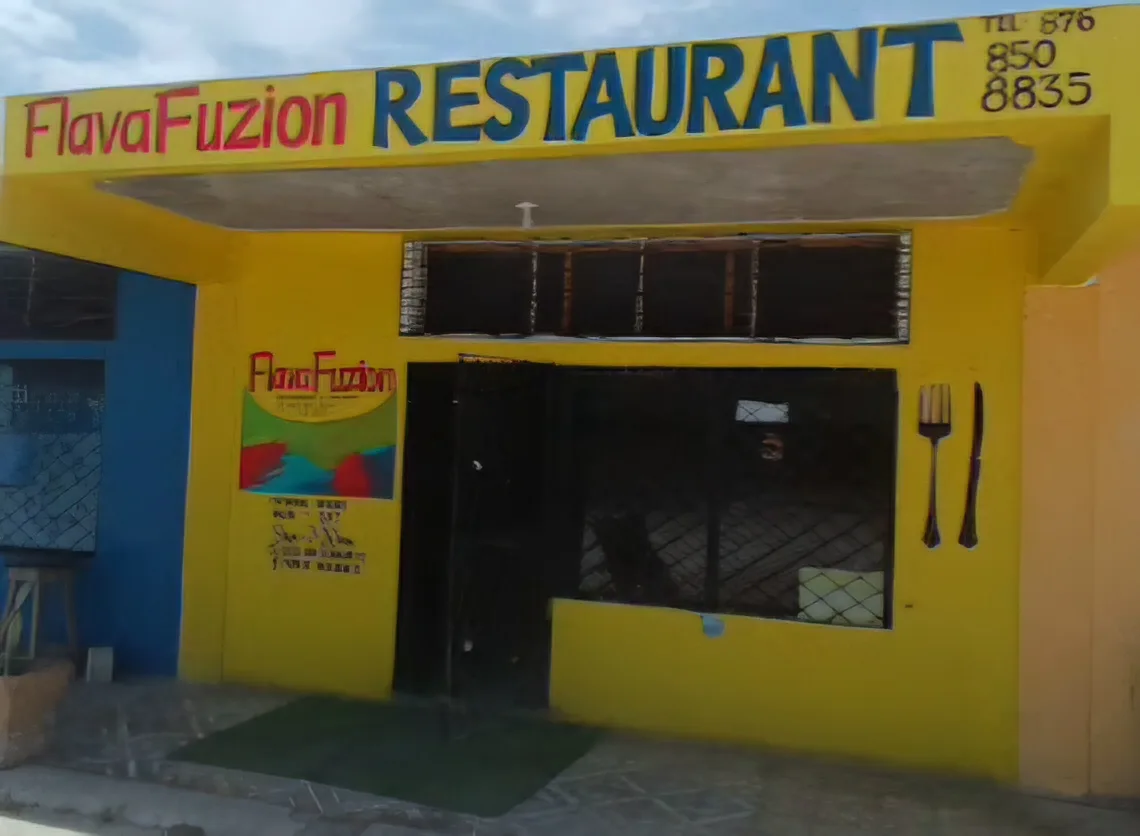 The front of Flava Fuzion: a bright yellow building with the sign FlavaFuzion Restaurant, Tel 876 850 8835, a painted FlavaFuzion board beside the door and a large fork and knife on the wall
