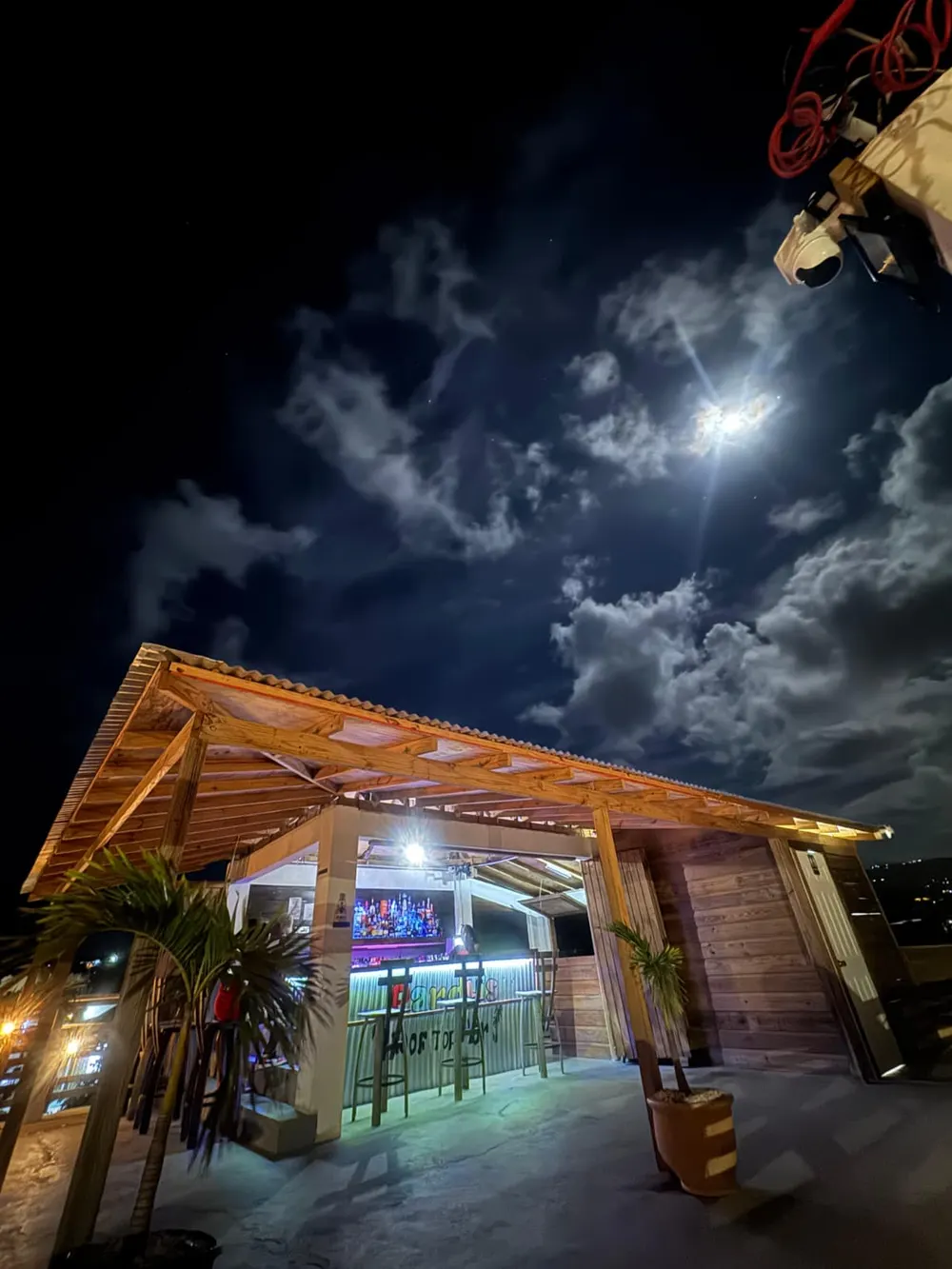 Pardy’s Rooftop Bar — The wooden roof of the bar lit from below, with a palm in front, under a moonlit sky of clouds