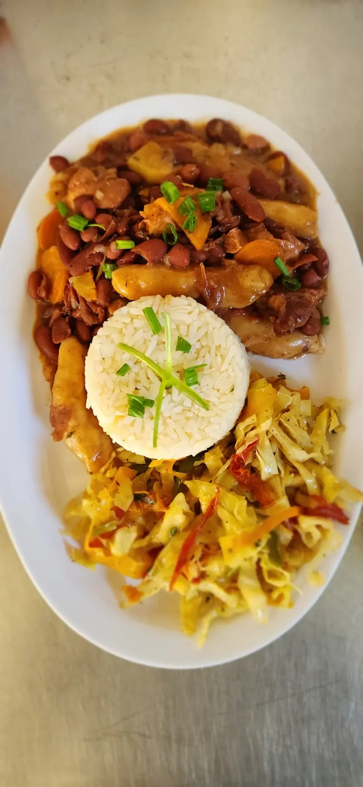 A plate of stew peas: red kidney beans stewed with spinners and carrots, a mould of white rice topped with scallion, and steamed cabbage with sweet peppers