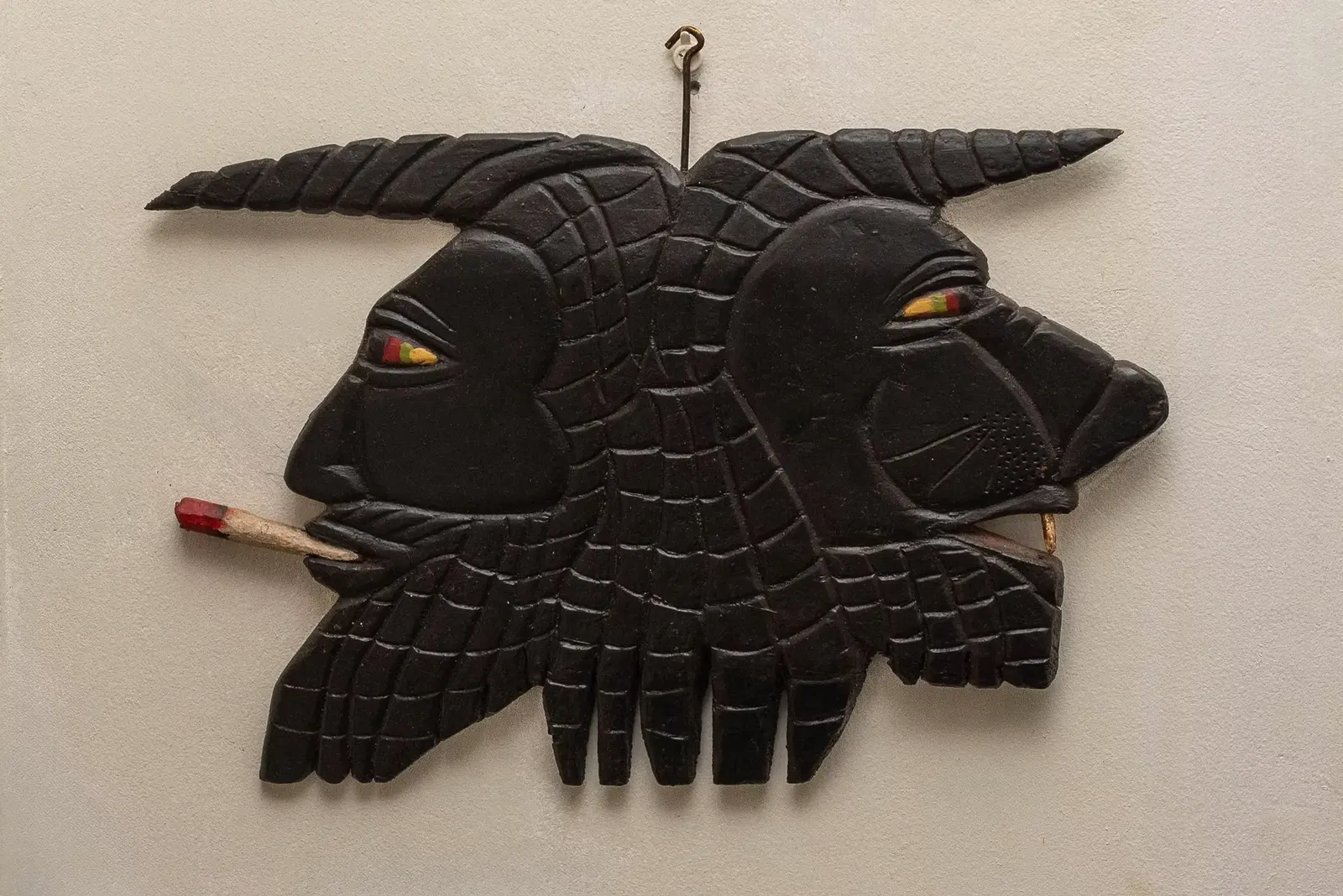 A black carved wooden wall piece of two profile faces with yellow eyes