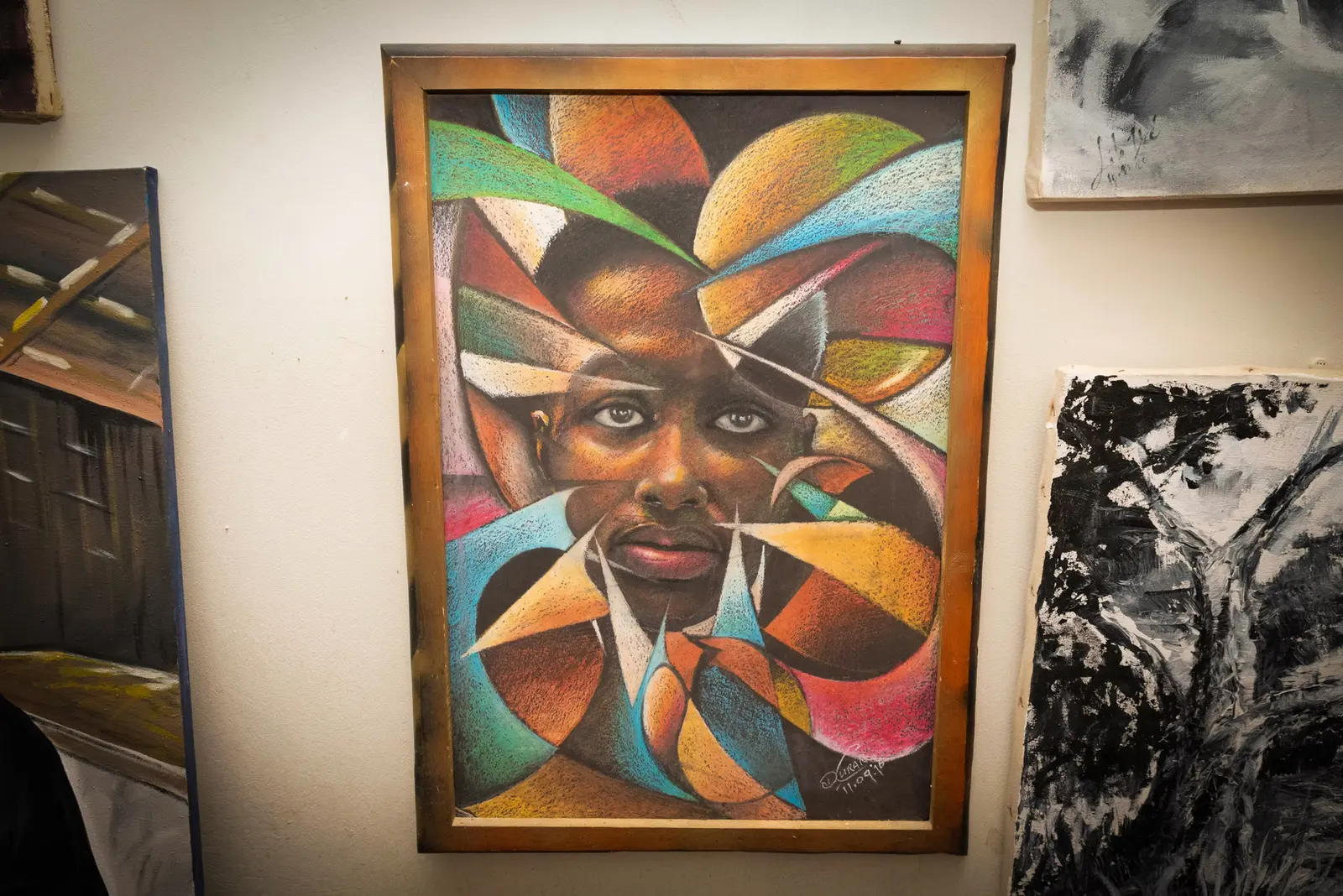A colourful, geometric portrait of a face in a wooden frame, hung among other canvases