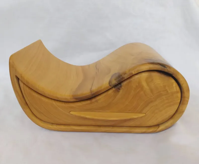 A yellow wooden jewellery box curved like a wave, with one drawer