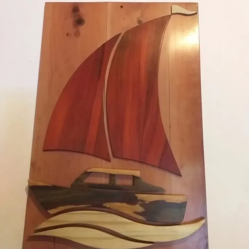 A wall panel of wood inlay: a motor yacht under two red sails on carved waves