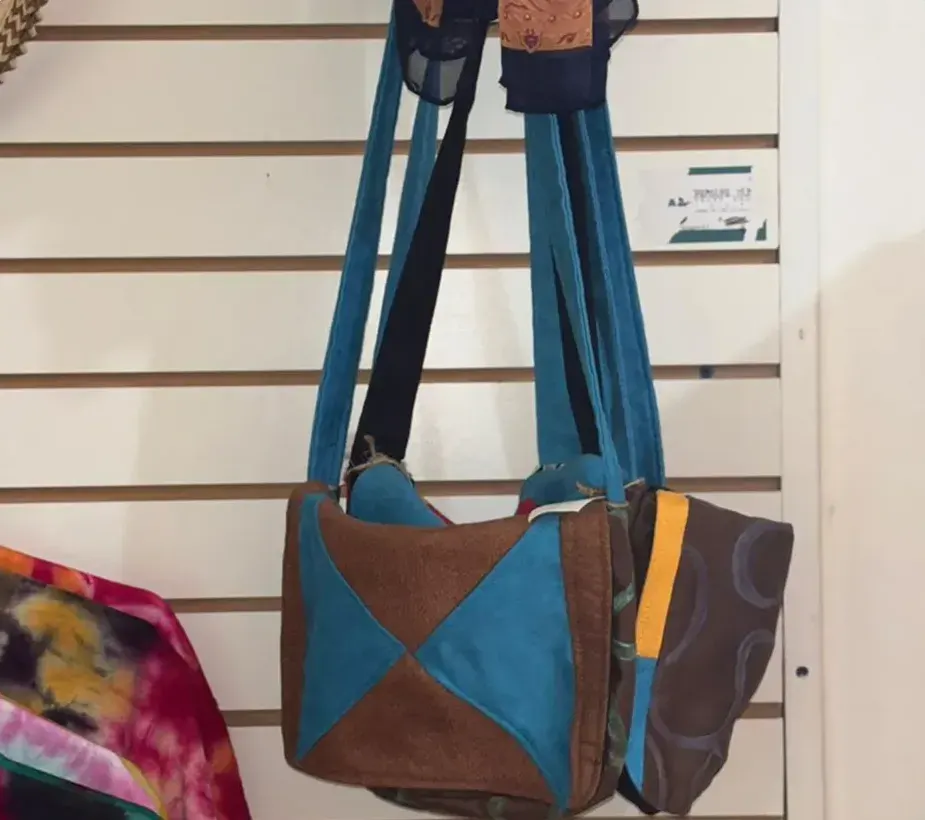 Shoulder bags sewn from patches of teal and brown suede, hanging on a slatted wall