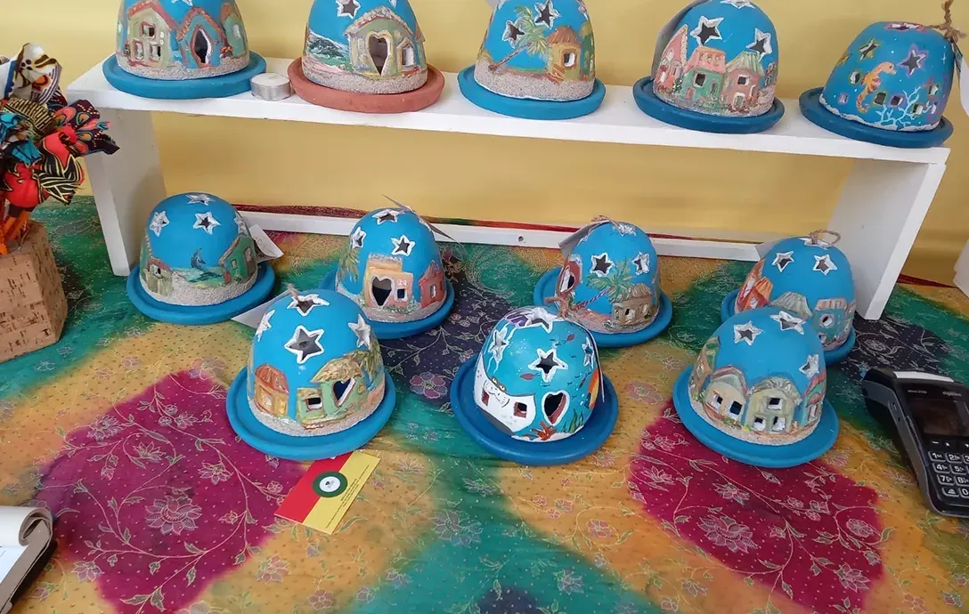 Two rows of Starlight lanterns, blue domes painted with Jamaican village houses, palm trees and sea creatures, with star and heart cut-outs, on a colourful tie-dyed cloth