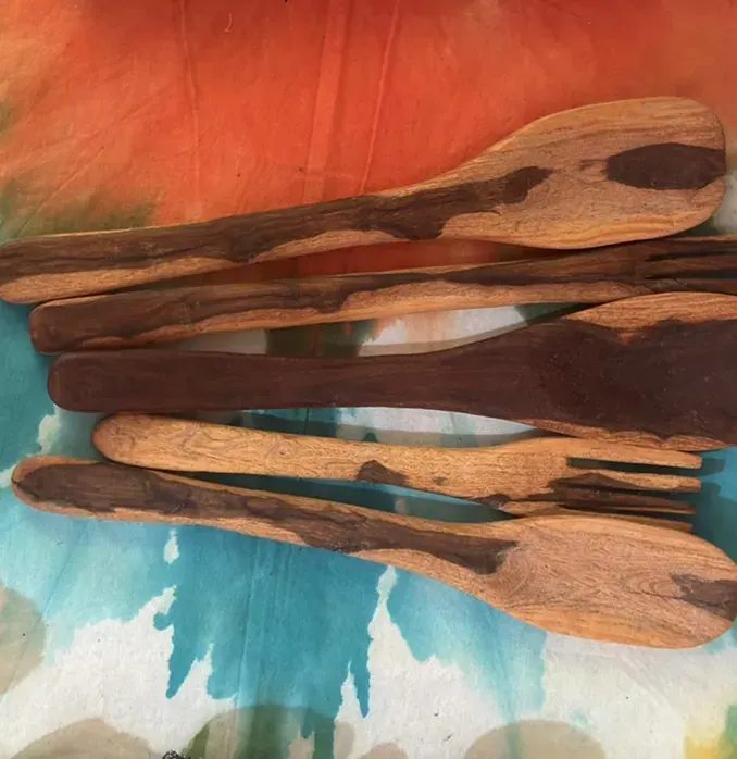 Five hand-carved wooden forks and spoons in dark and light wood on an orange and teal tie-dyed cloth
