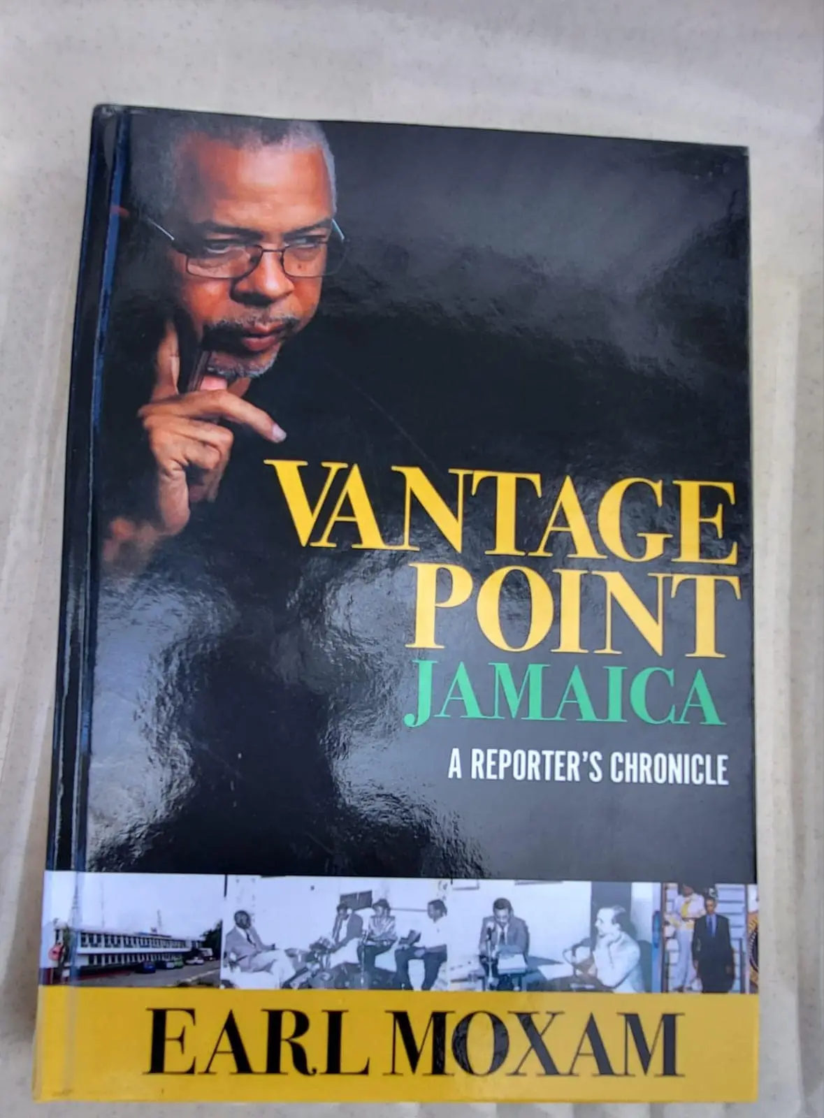 The cover of Vantage Point Jamaica: A Reporter’s Chronicle by Earl Moxam: his portrait on black, the title in gold and green, and a strip of archive photographs above his name on a gold band